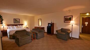 Una habitación de hotel con una cama, dos sillones, una mesita, un televisor y una lámpara.