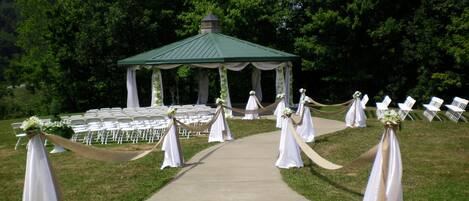 A gazebo with a green roof and white columns, surrounded by white chairs and a pathway leading to it.