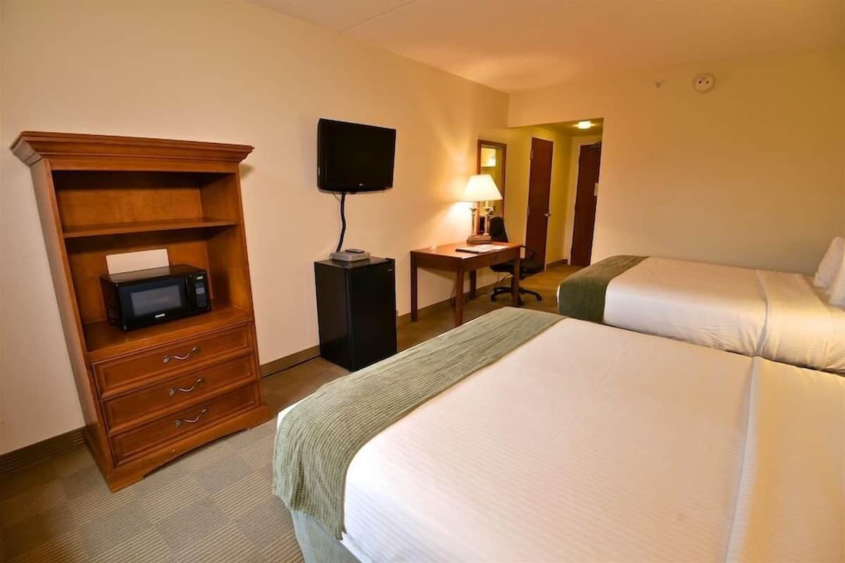 A hotel room with two beds, a desk with a lamp, a television, and a microwave.
