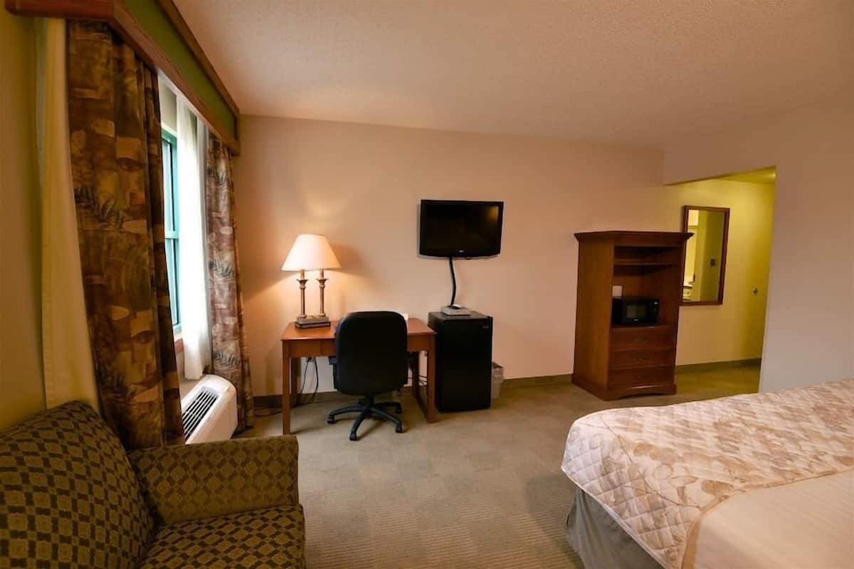 A hotel room with a bed, a desk with a chair, a television, a small cabinet, and a window with curtains.