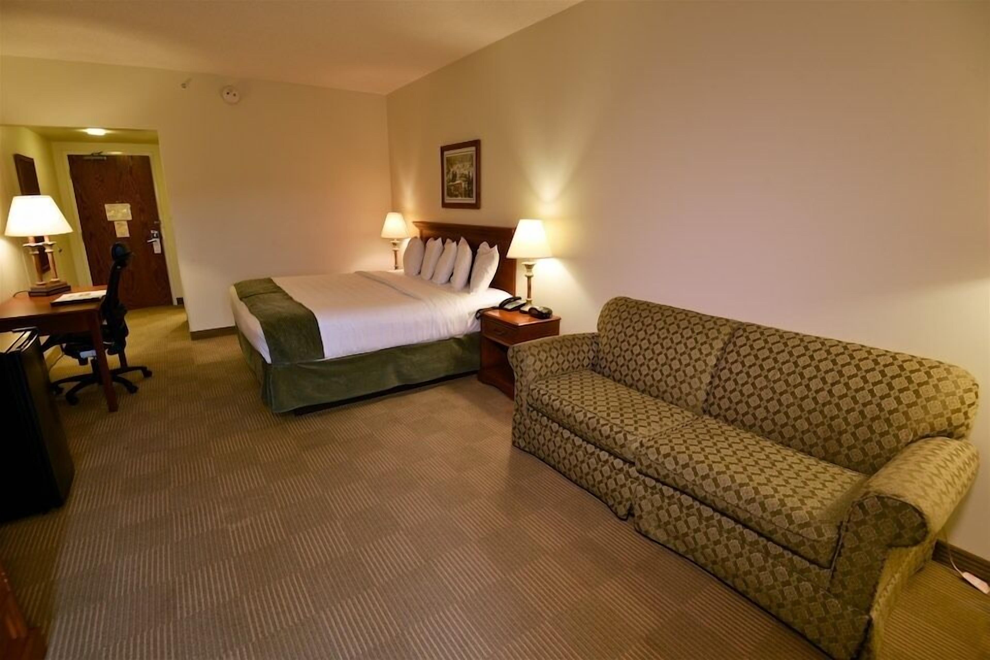Une chambre d’hôtel avec un lit, deux lampes de chevet, un canapé à motifs, un bureau avec une lampe et une chaise.