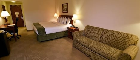 Une chambre d’hôtel avec un lit, deux lampes de chevet, un canapé à motifs, un bureau avec une lampe et une chaise.