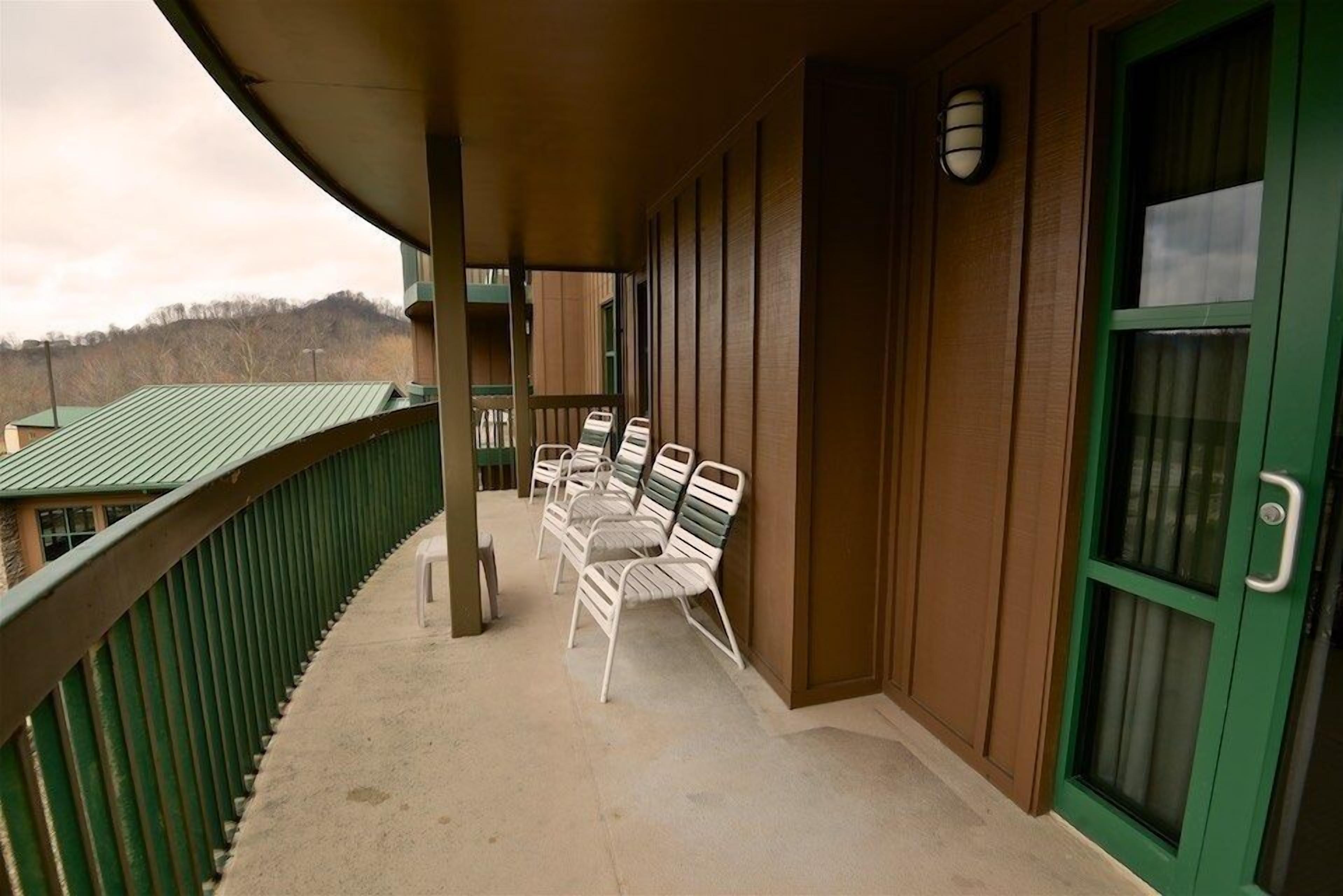 A covered balcony with a row of white metal chairs and a wooden wall with a green door.