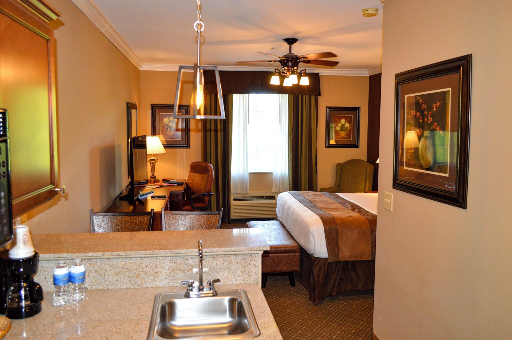 A hotel room with a bed, a desk, a chair, a sink, and a ceiling fan.