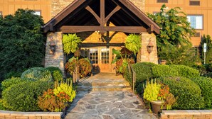 A stone pathway leading to a building entrance with a wooden overhang and potted plants on either side. - The Lodge at Flat Rock (Flat Rock)
