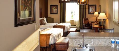 A hotel room with two beds, a desk, a chair, a sink, and a ceiling fan.