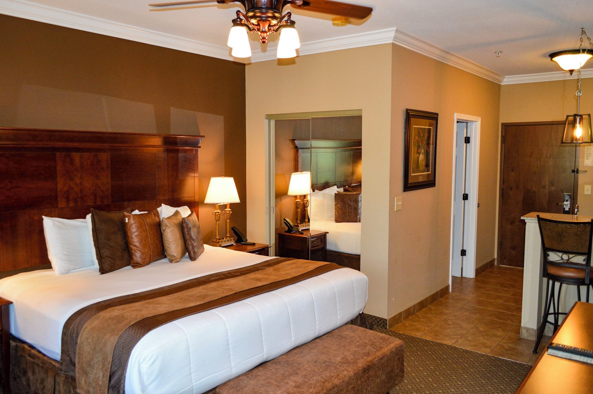 A hotel room with a large bed, two bedside tables with lamps, a desk with a chair, and a door leading to a bathroom.