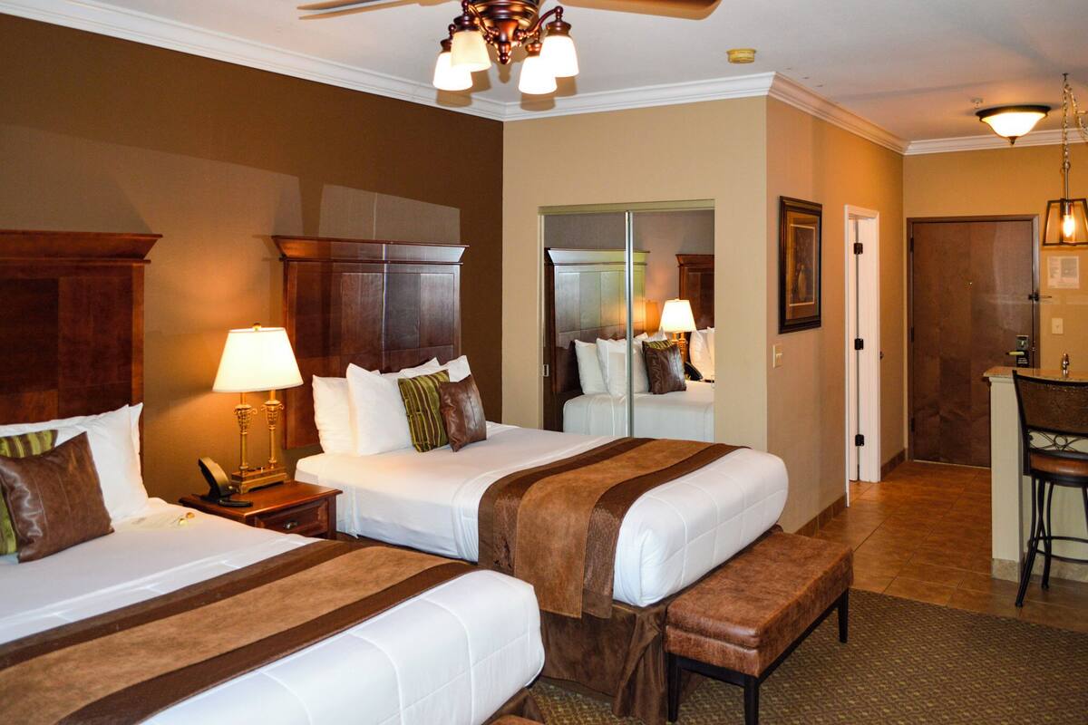 A hotel room with two beds, a desk, and a bathroom.