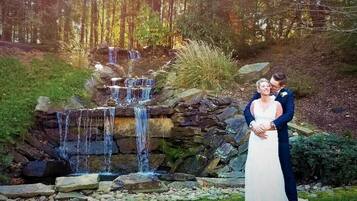 A couple standing in front of a waterfall with a stone wall and greenery in the background.