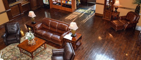 A lobby with a brown leather sofa, two armchairs, a wooden coffee table, and a reception desk.