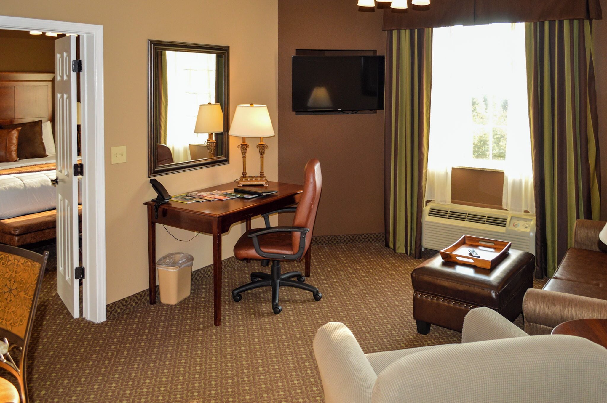 A hotel room with a bed, desk, chair, TV, and a window with curtains.