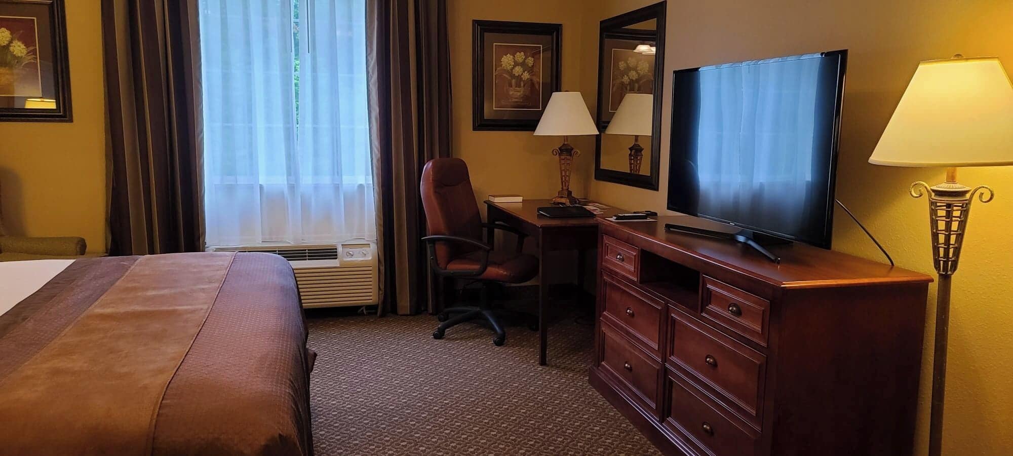 Habitación de hotel con cama, escritorio, silla, televisor, cómoda y lámparas.