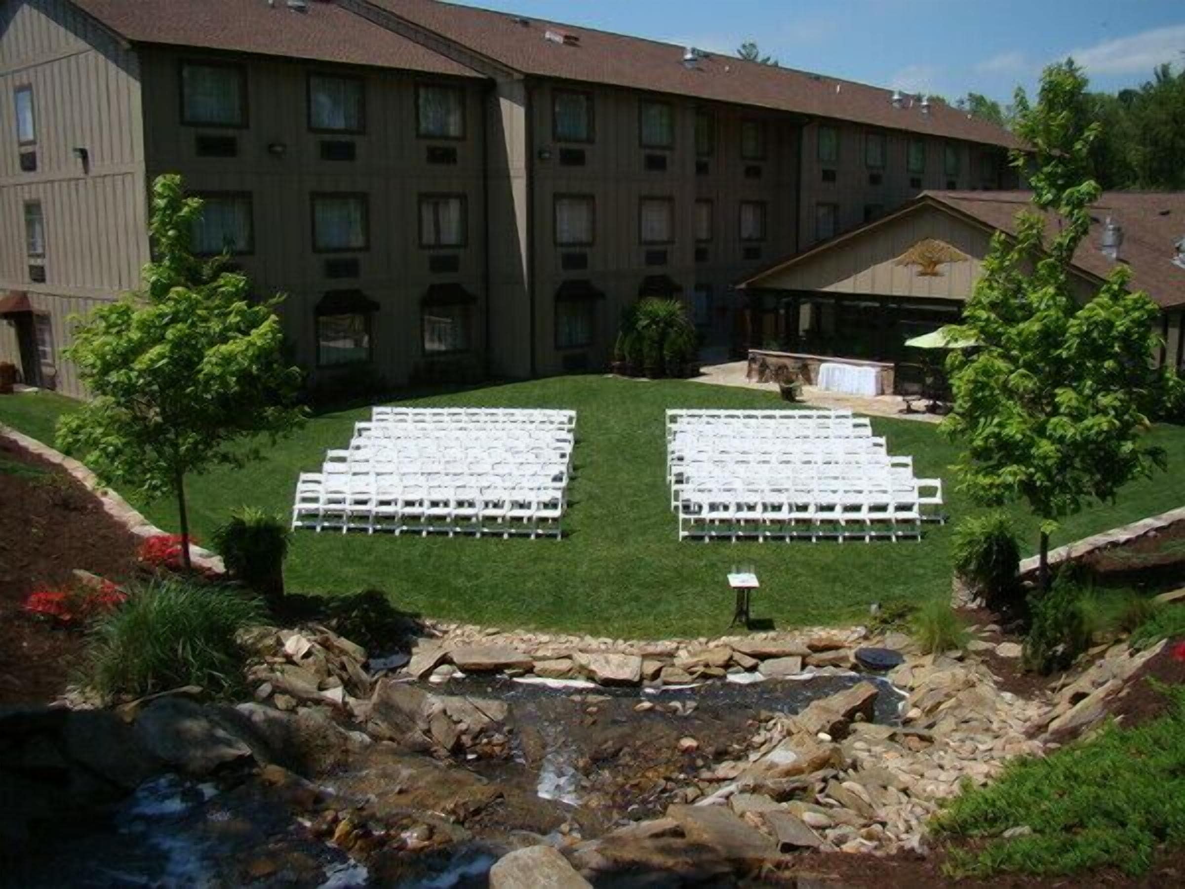 A courtyard with two rows of white chairs arranged for an event, a building with multiple windows, and a small waterfall feature.