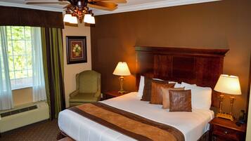 A hotel room with a large bed, two bedside tables with lamps, a ceiling fan, a window with curtains, and a framed picture on the wall.