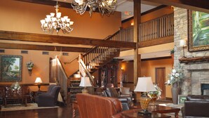 A spacious lobby with a grand staircase, leather furniture, and a stone fireplace. - The Lodge at Flat Rock (Flat Rock)