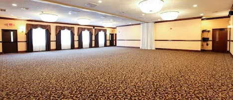 Una sala amplia con alfombra y piso estampado, varias ventanas con cortinas y un candelabro.