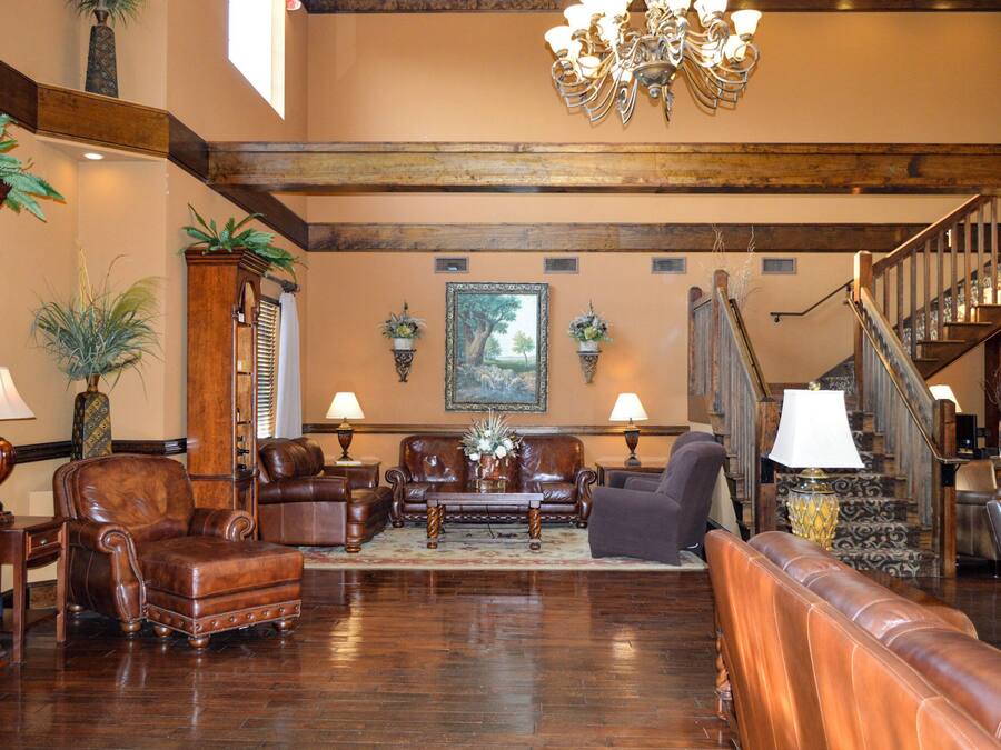 A spacious living room with leather furniture, a chandelier, and a staircase.