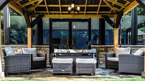 A covered patio with wicker furniture and a stone wall backdrop. - The Lodge at Flat Rock (Flat Rock)