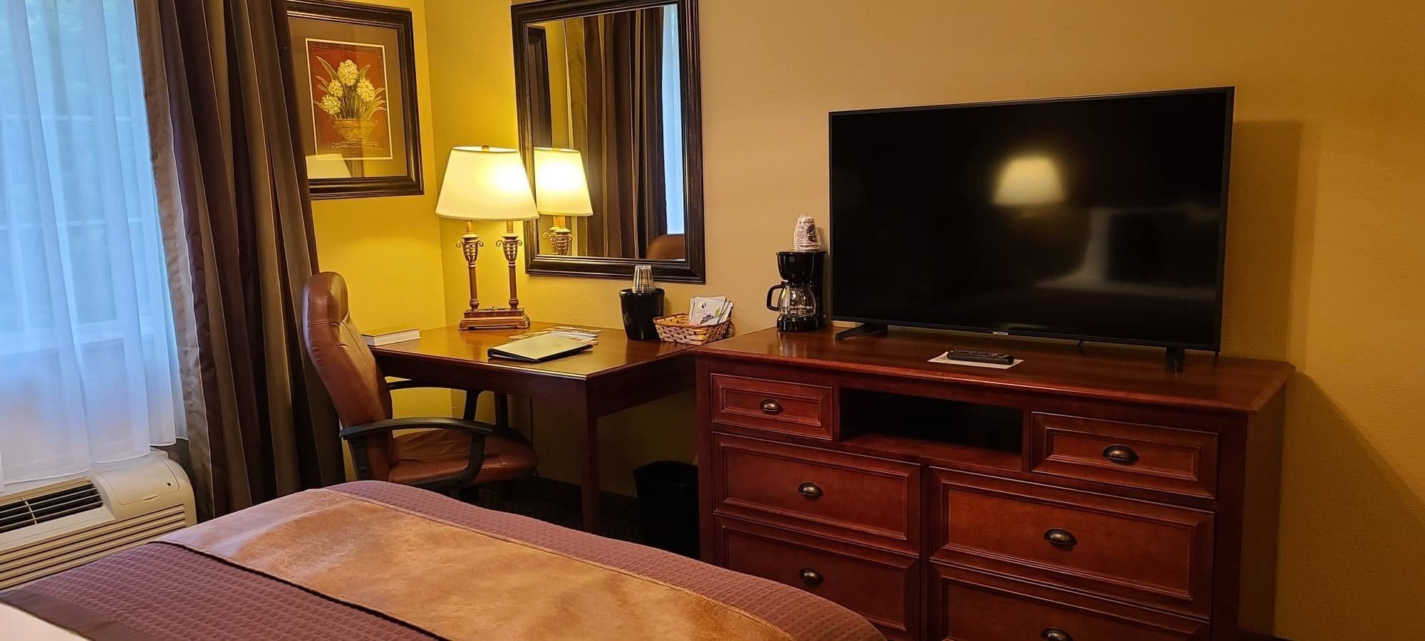 Una habitación de hotel con una cama, un escritorio con silla, un televisor, una lámpara y un aparador.