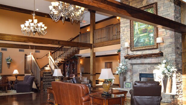 A spacious lobby with a grand staircase, leather sofas, chandeliers, and a stone fireplace. - The Lodge at Flat Rock (Flat Rock)