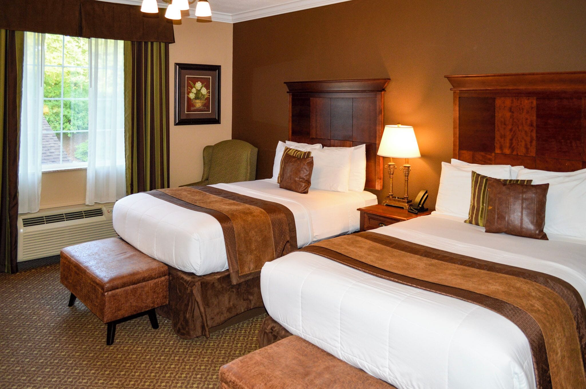 A hotel room with two beds, a chair, a lamp, and a window with curtains.