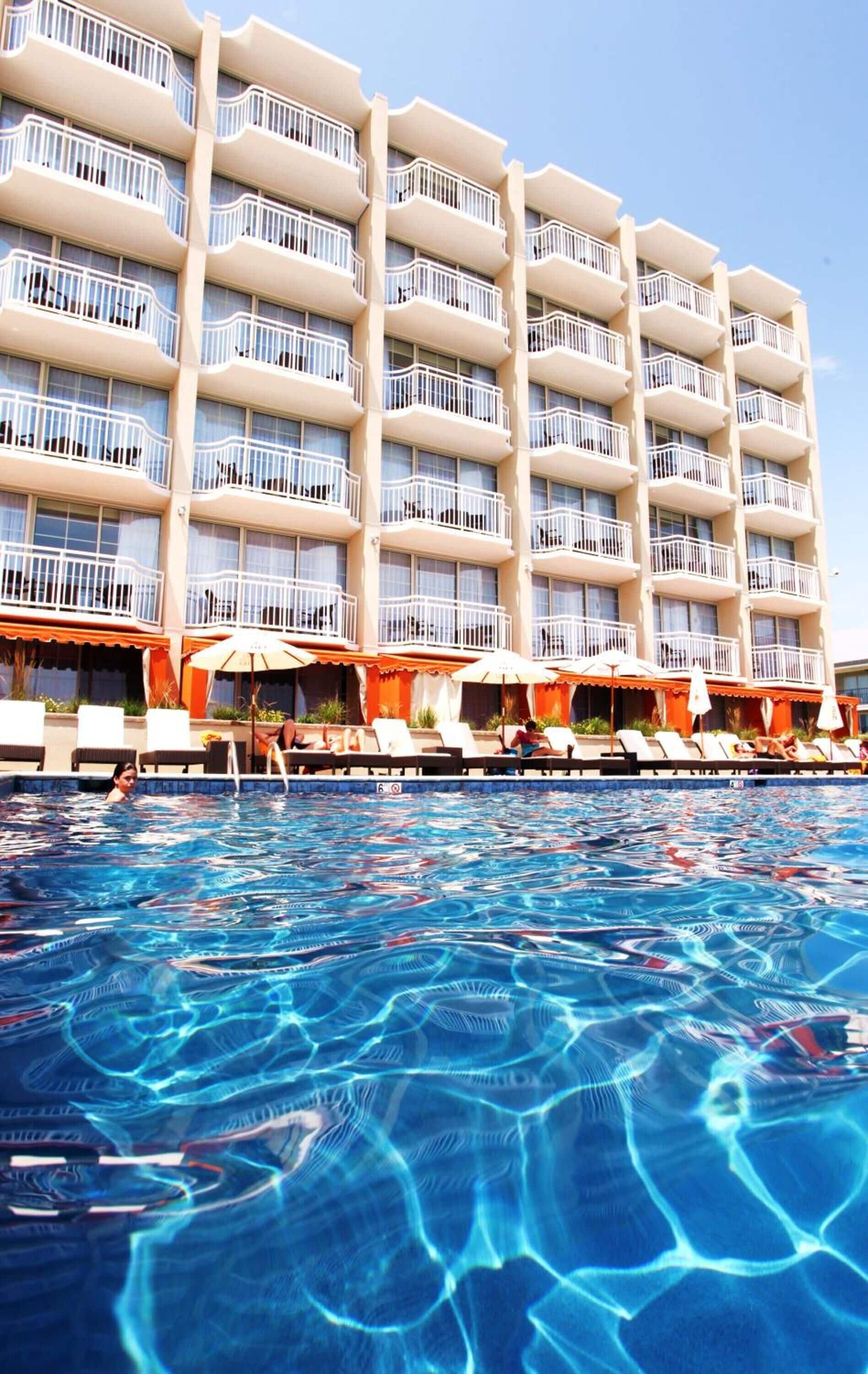 A hotel with multiple balconies, a swimming pool, and sun loungers.