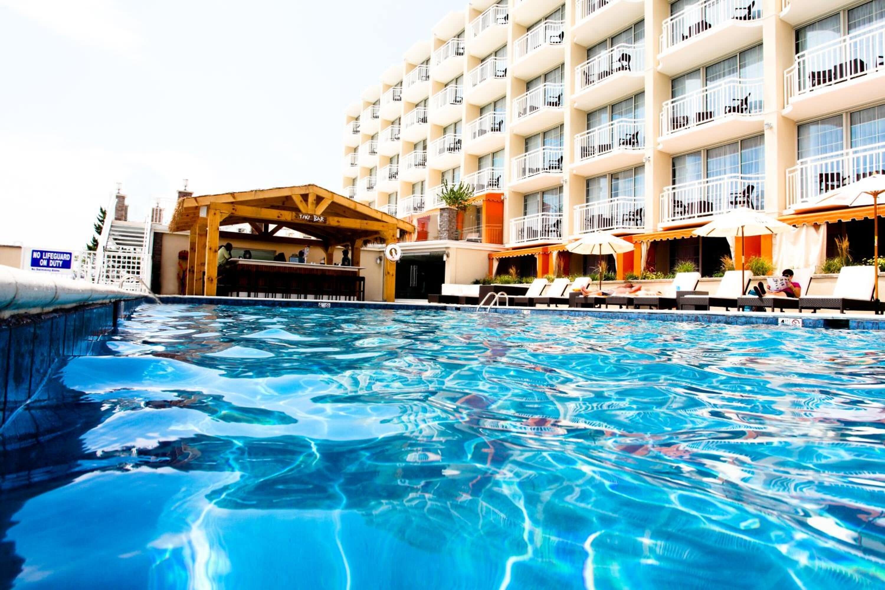 Ein Hotelpoolbereich mit Bar, Liegestühlen und einem mehrstöckigen Gebäude mit Balkonen.