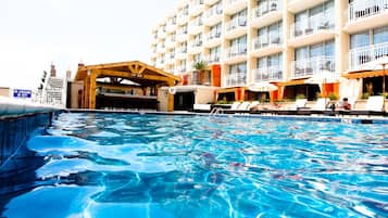 Ein Hotelpoolbereich mit Bar, Liegestühlen und einem mehrstöckigen Gebäude mit Balkonen.