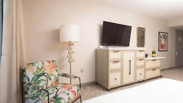 Una habitación de hotel con una cama, un sillón floral, un aparador, un televisor y un espejo.