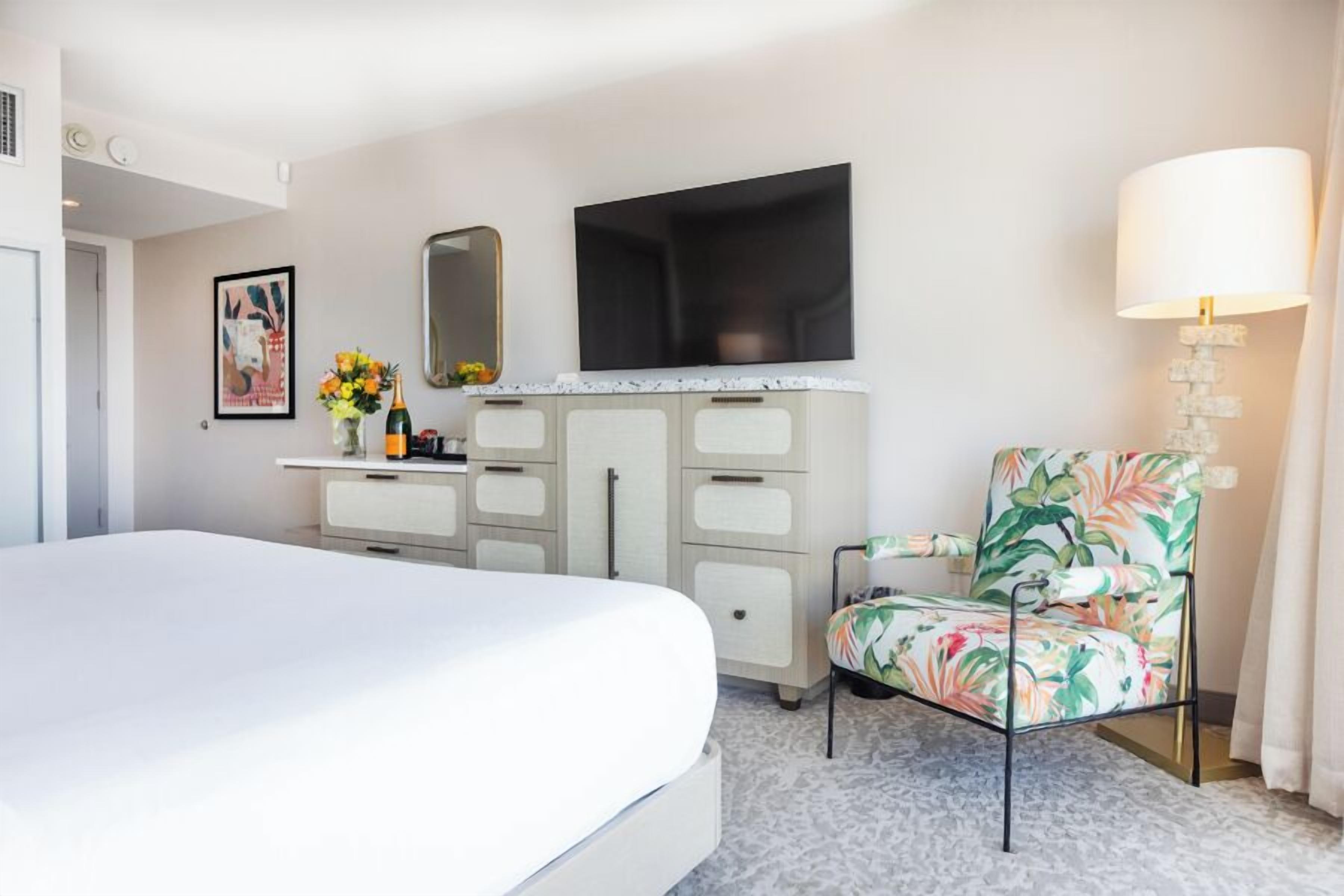A hotel room with a bed, a dresser, a television, a chair, and a lamp.
