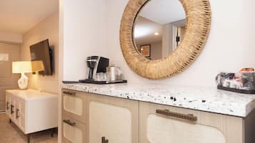 A hotel bathroom with a round mirror, a coffee machine, and a sink.