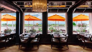 An indoor dining area with tables and chairs, large windows, and orange umbrellas. - Ocean Club Hotel (Cape May)