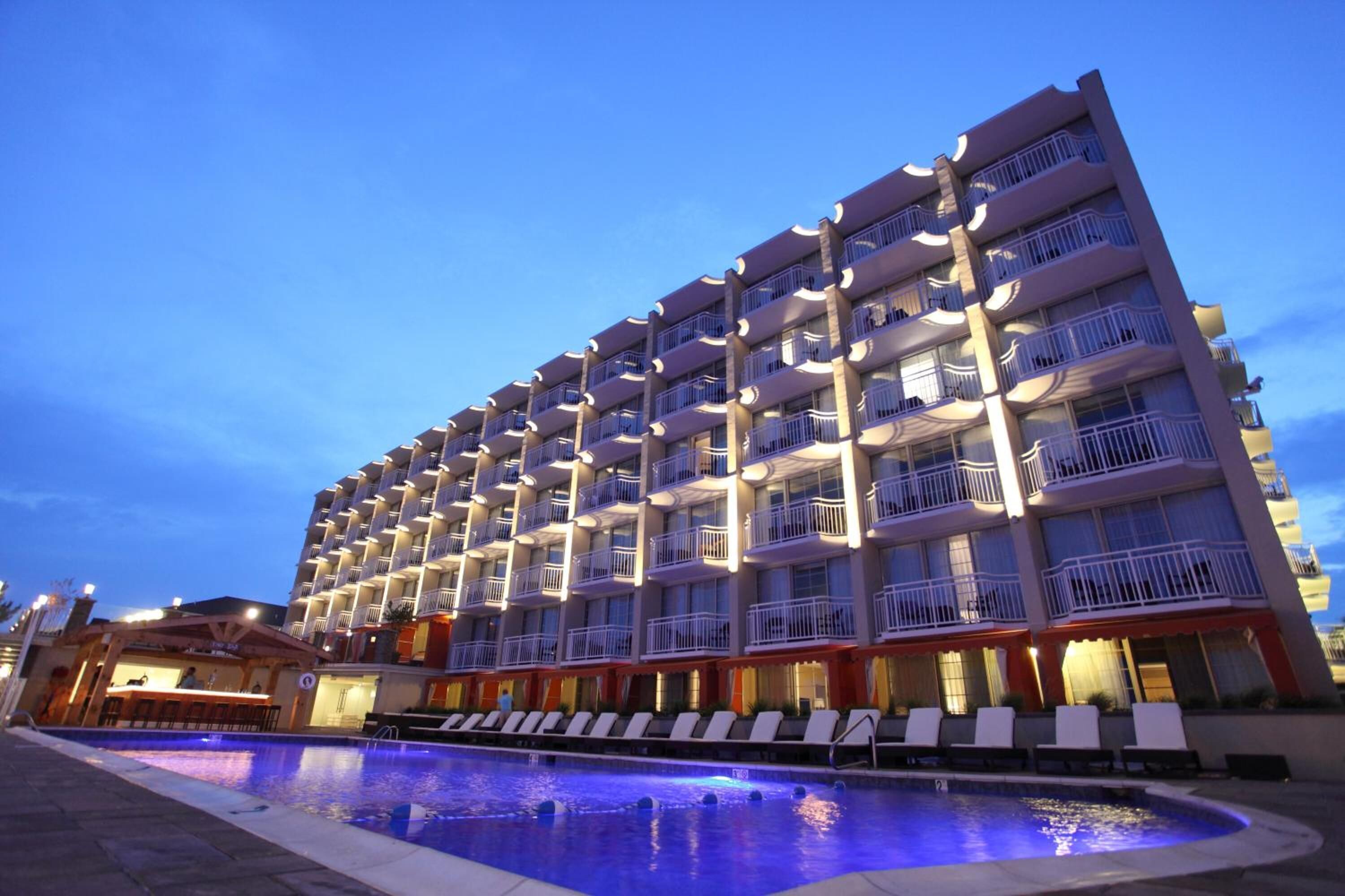 Um hotel com vários andares, varandas, piscina com espreguiçadeiras e área de bar.