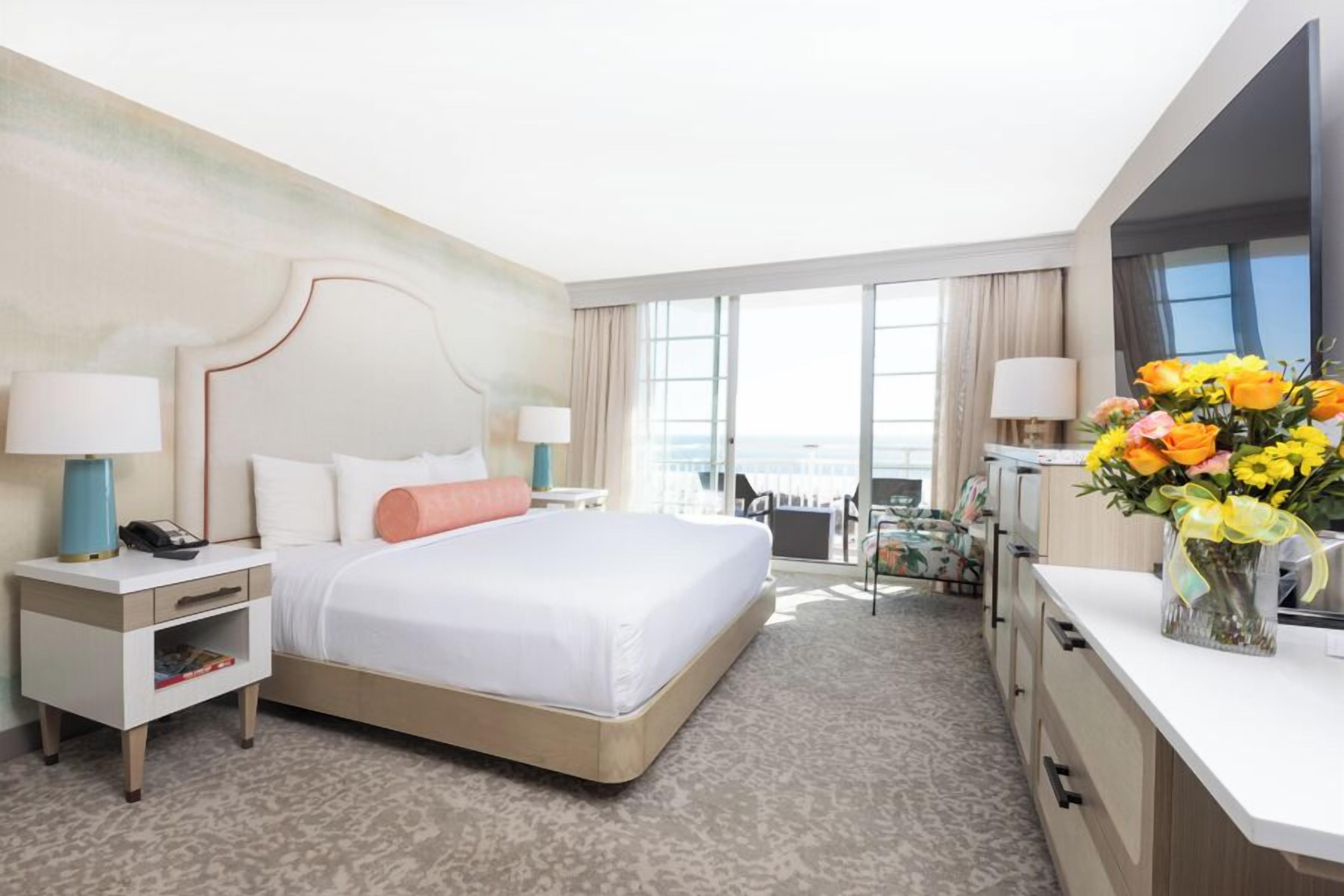 A hotel room with a large bed, bedside tables, a desk, and a view of the ocean.