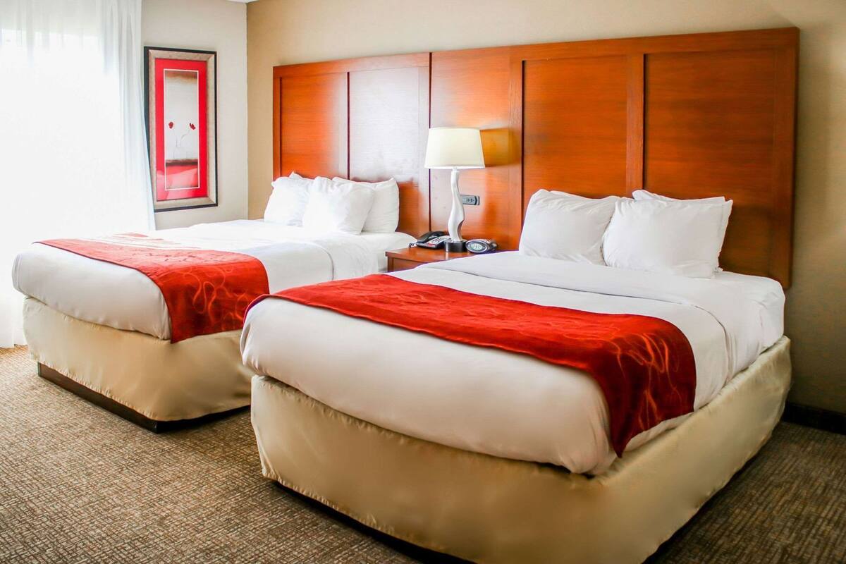 A hotel room with two beds, a wooden headboard, a bedside lamp, and a framed picture on the wall.