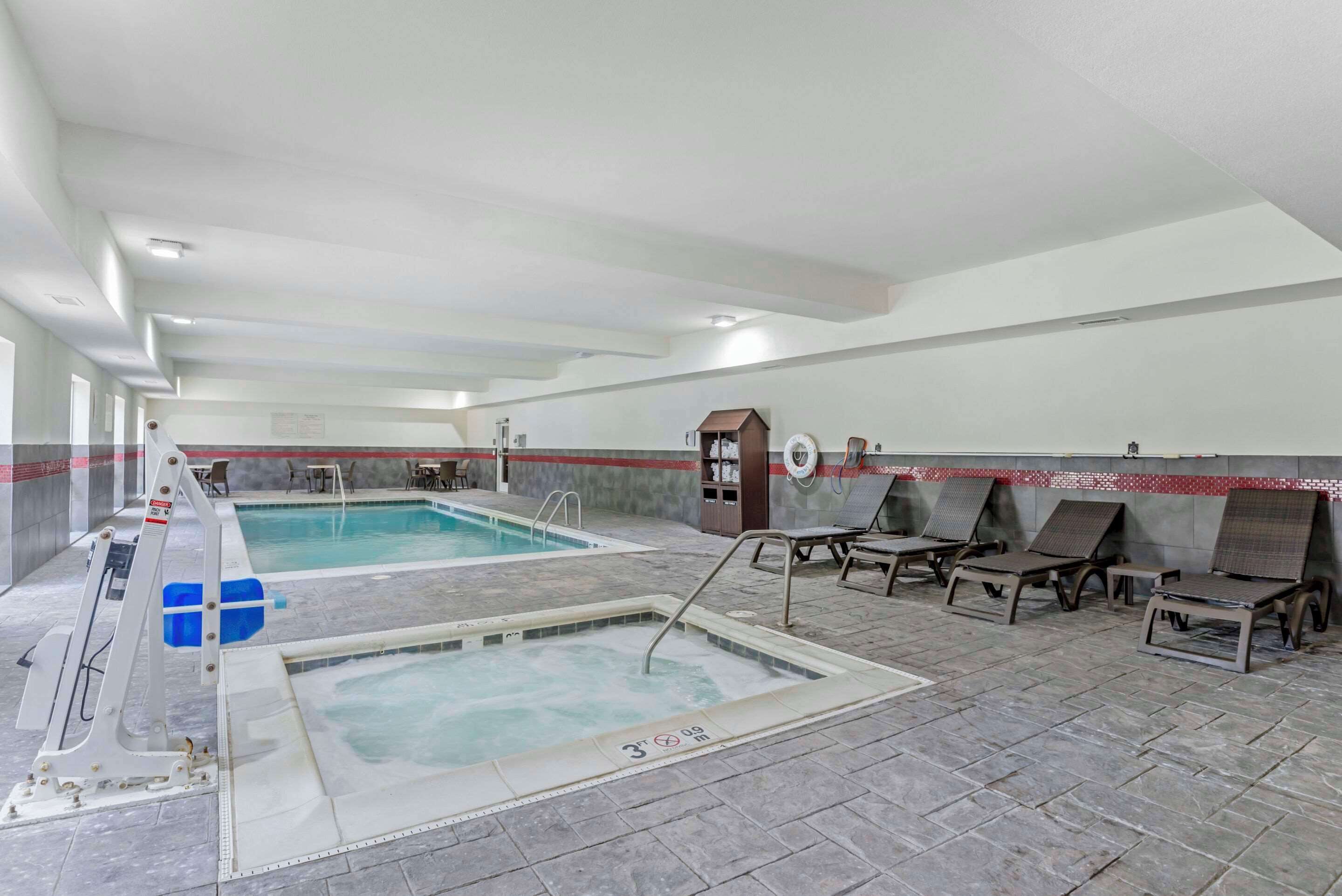 Zona de piscina con dos piscinas, sillas de descanso y un vestuario.