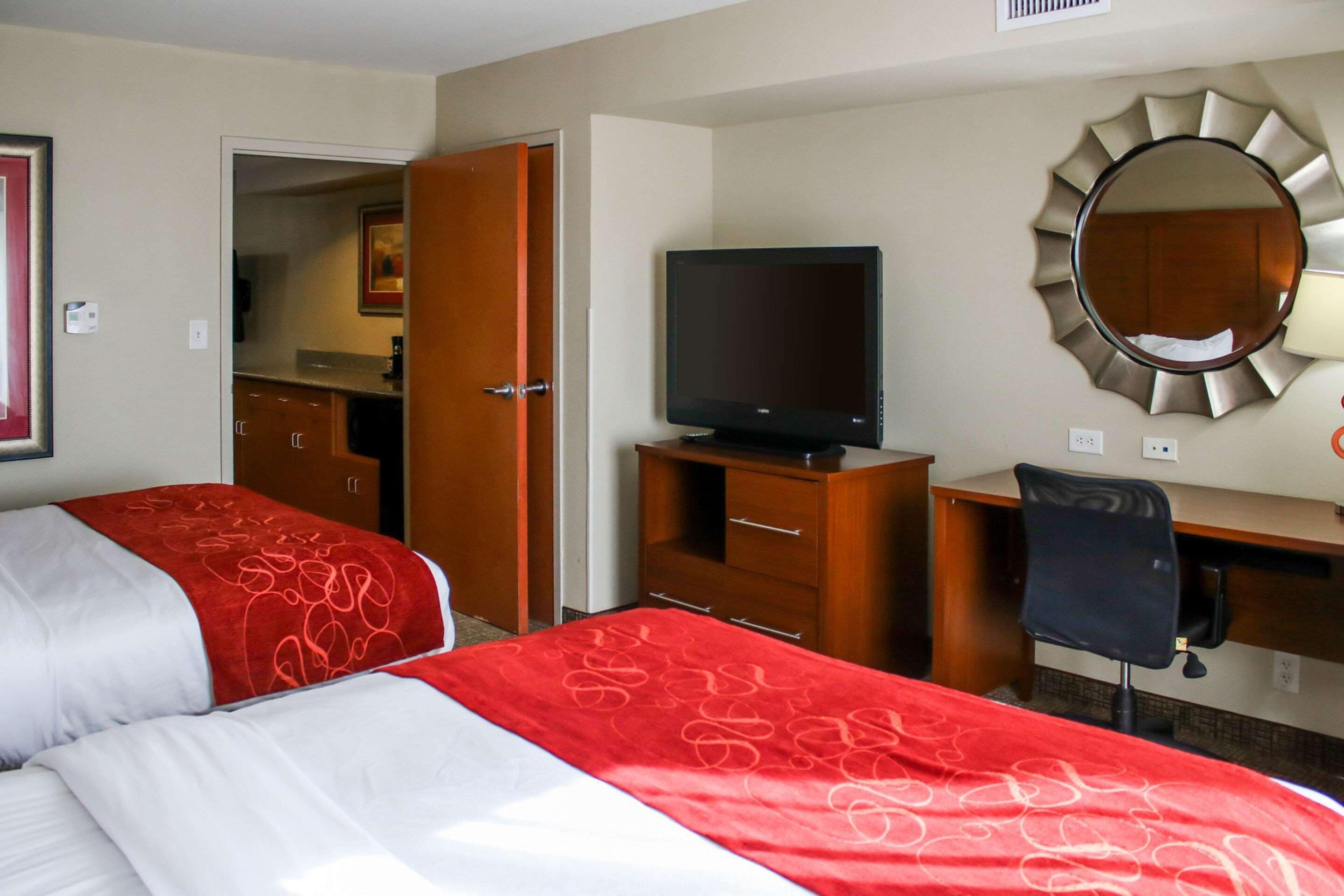 A hotel room with two beds, a TV, a desk, and a mirror.