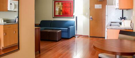 Un espacio habitable compacto con kitchenette, un sofá azul, una mesa de comedor y piso de madera.