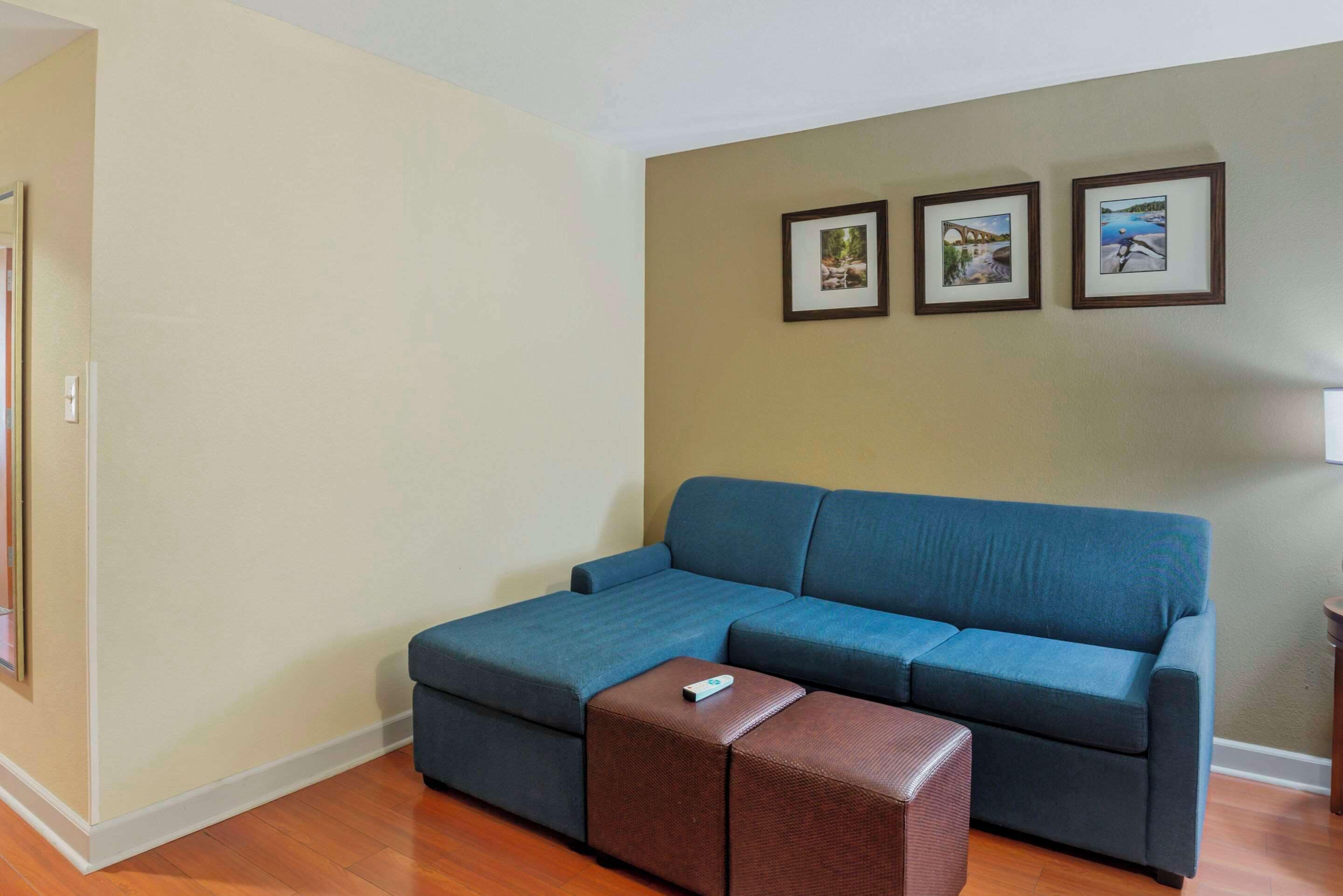 Ein Wohnzimmer mit einem blauen Moduls Sofa, einem braunen Hocker und drei gerahmten Bildern an der Wand.
