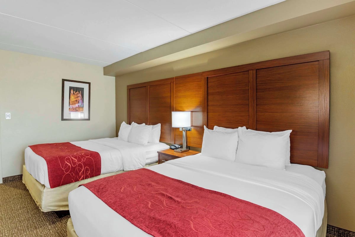 A hotel room with two beds, a wooden headboard, a nightstand with a lamp, and a framed picture on the wall.