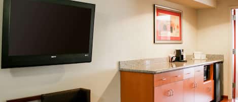A modern kitchen with a flat-screen TV, a framed picture, a sink, and a bench.