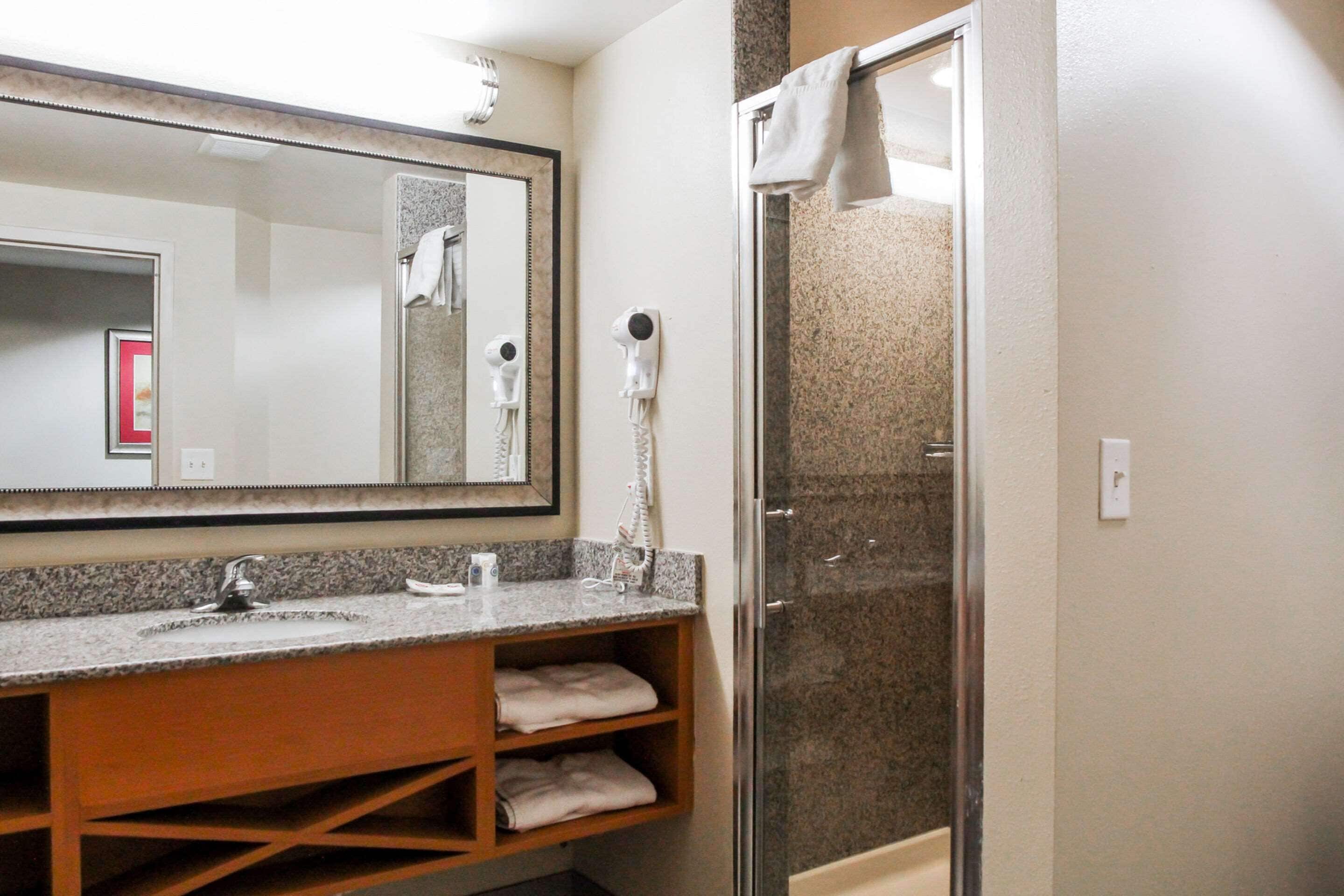 A bathroom with a granite countertop, a large mirror, a hairdryer, and a shower enclosure.