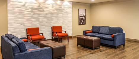 A modern lounge area with blue sofas, orange chairs, and wooden ottomans on a wooden floor.