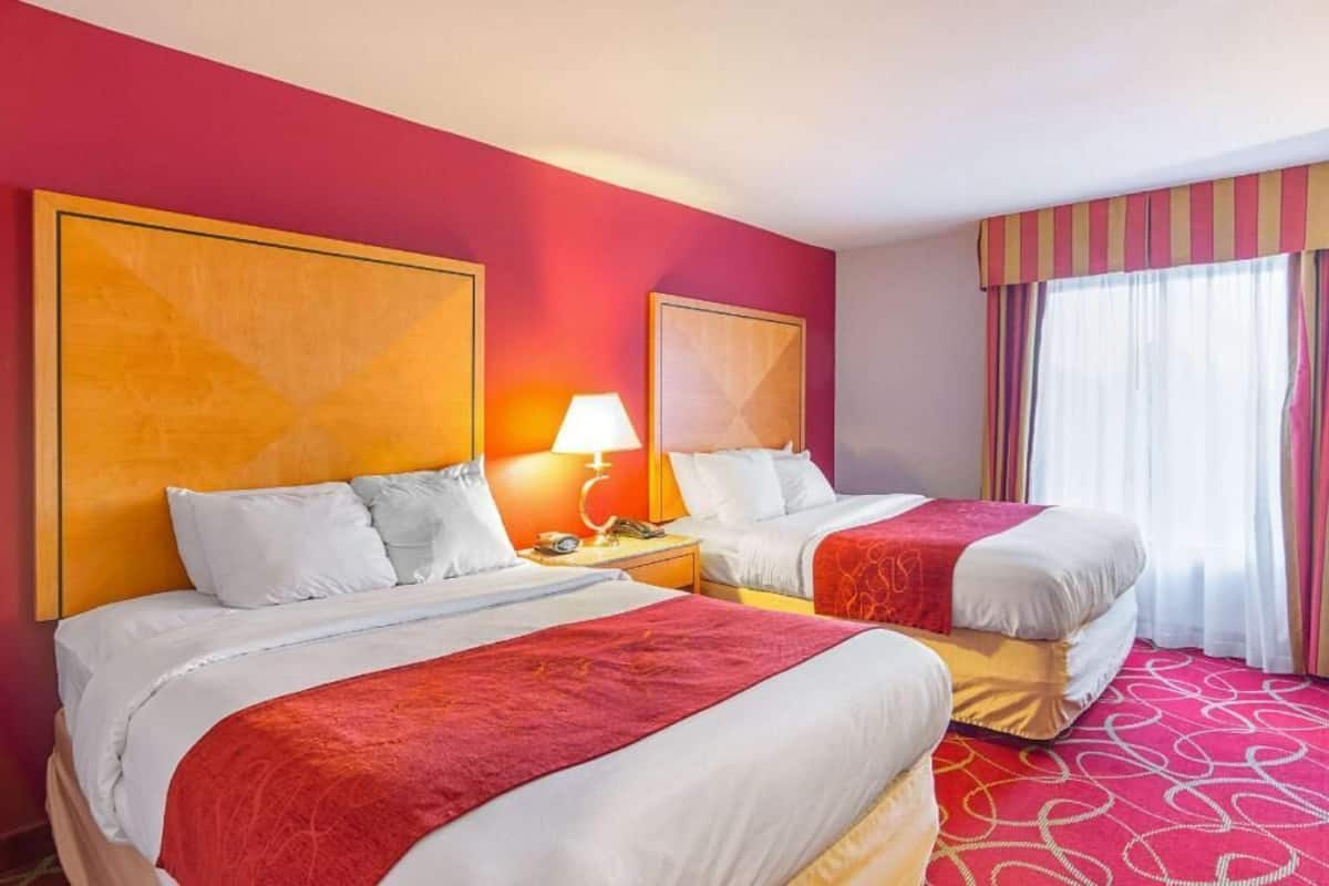 A hotel room with two beds, a large window with curtains, and a patterned carpet.