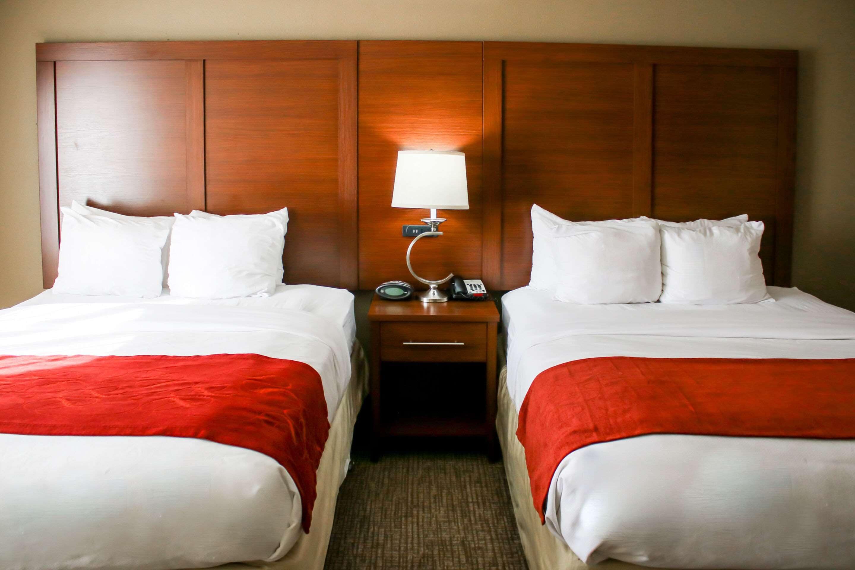 Ein Hotelzimmer mit zwei Betten, jeweils mit weißer Bettwäsche und roten Zudecken. Es gibt ein Holz-Kopfteil, einen Nachttisch mit einer Lampe und ein Telefon.