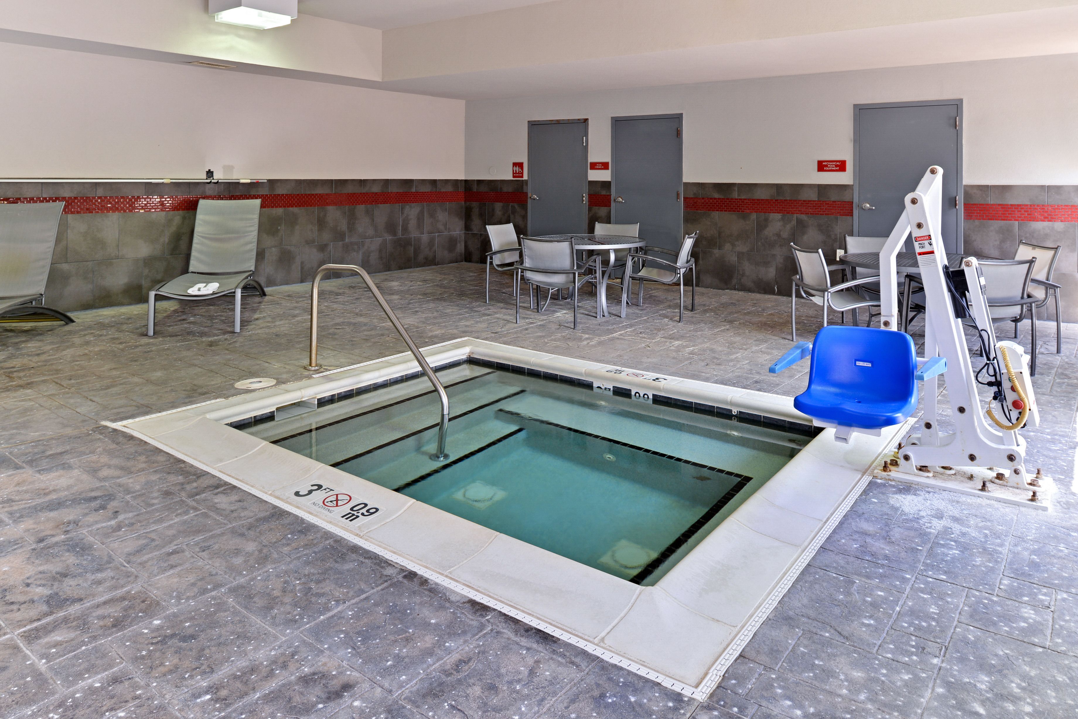 An indoor swimming pool with a tiled floor, a pool table, and several chairs.