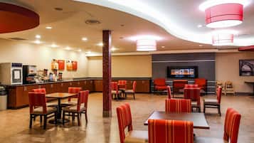 A hotel lobby with a central bar area, multiple seating arrangements, and a television screen.