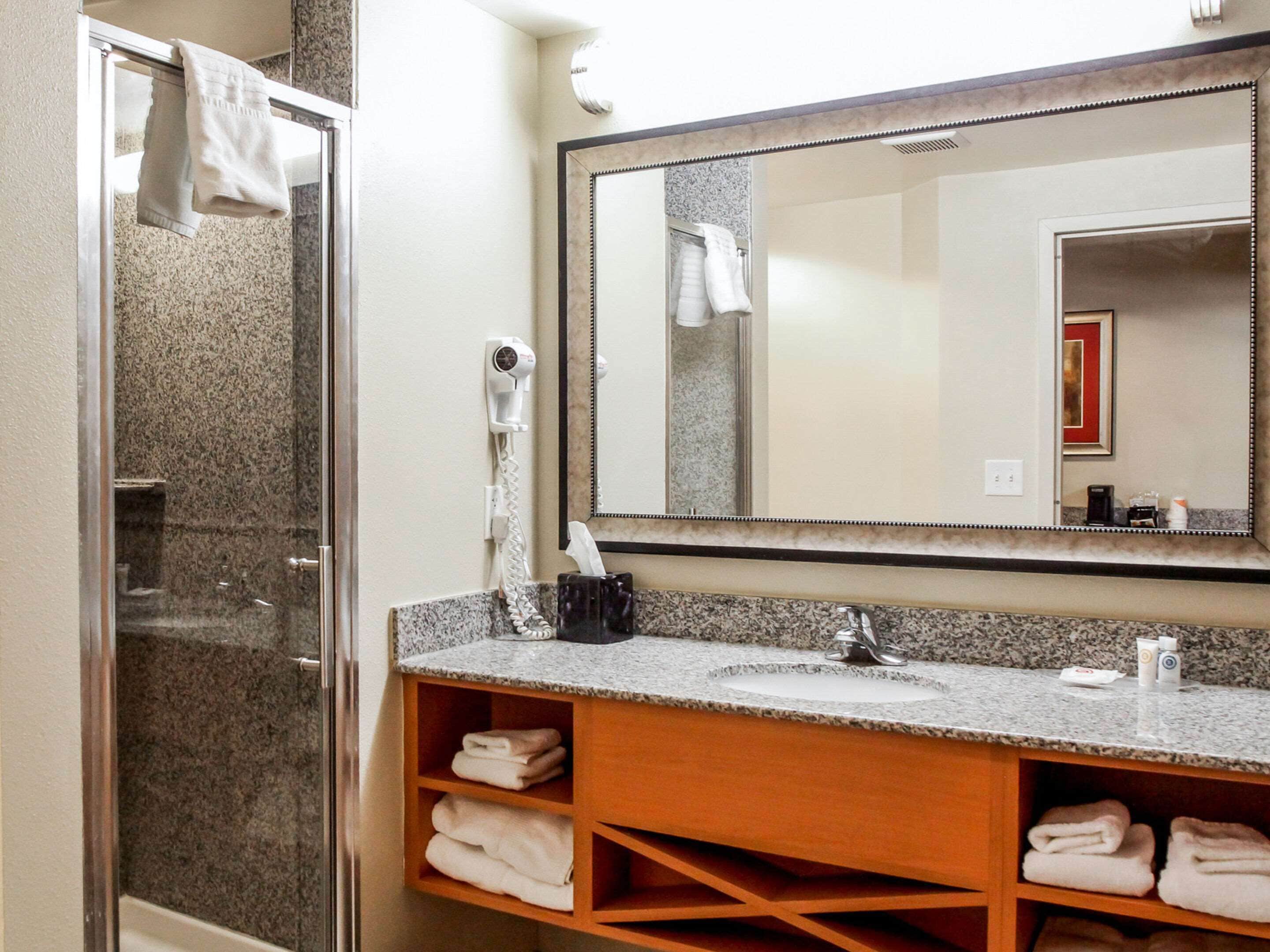 A bathroom with a shower, a sink, a mirror, and a towel rack.