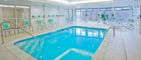 Una piscina interior con agua cristalina, rodeada de sillas de descanso y un cartel que indica 'No hay socorrista de servicio'.