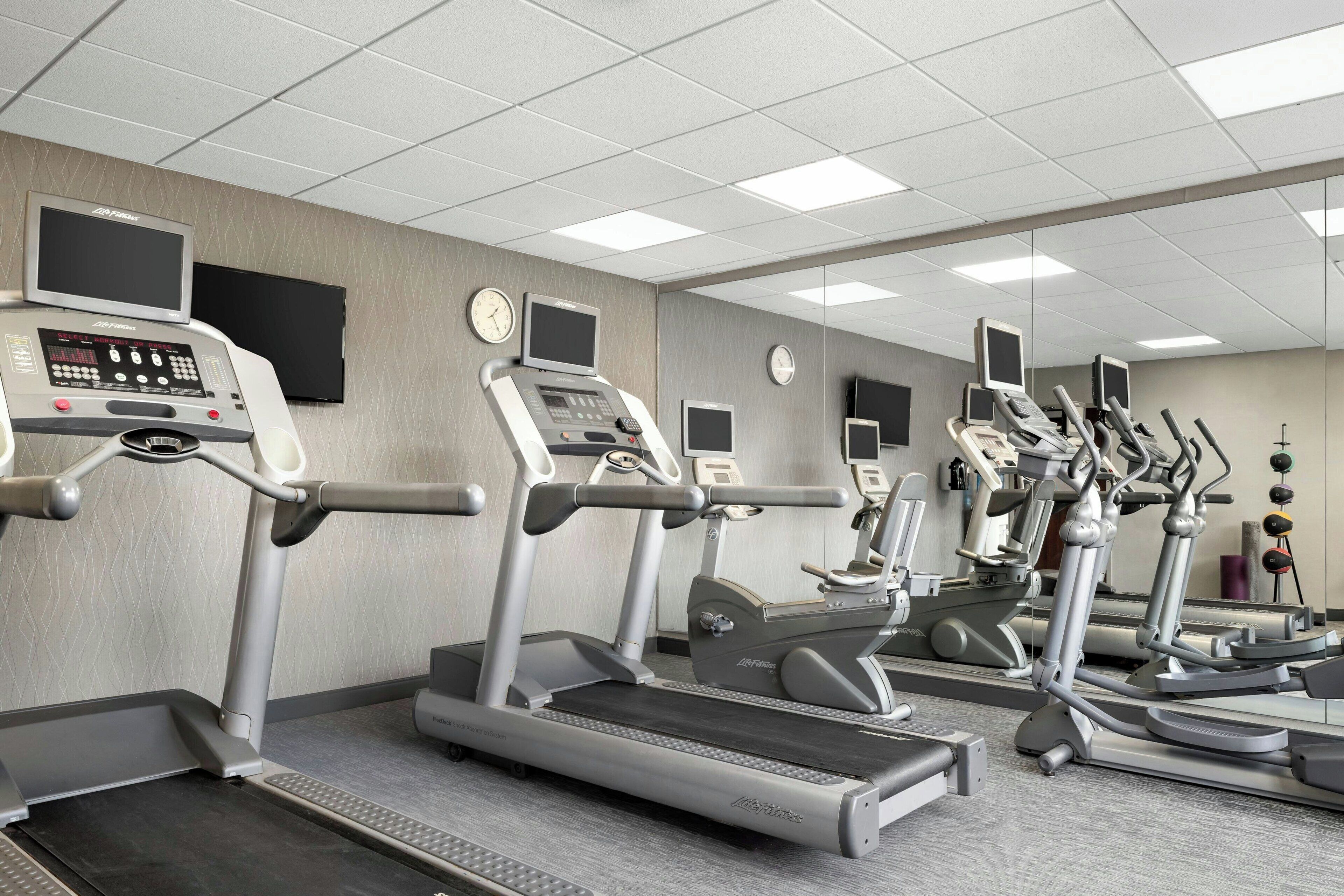 Ein Fitnessstudio mit Laufbändern, Crosstrainern und einem digitalen Bildschirm, der Trainingsdaten anzeigt.